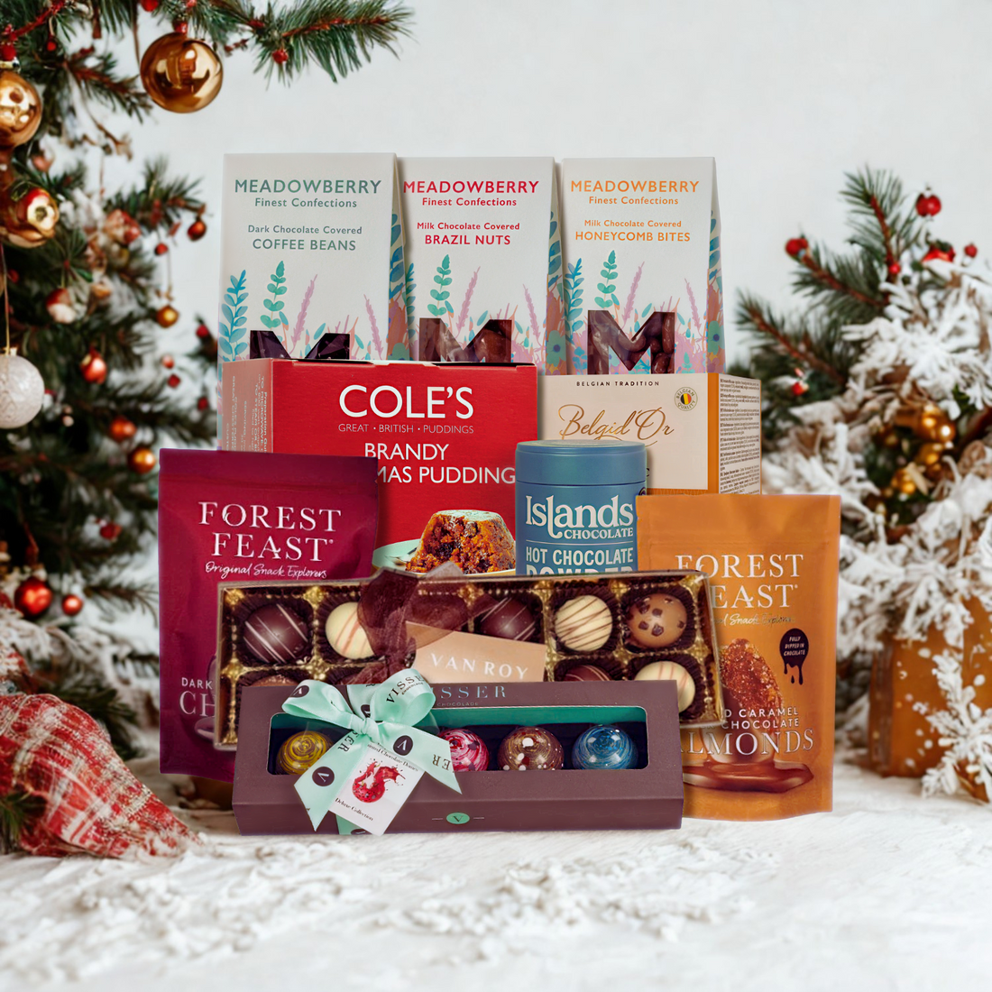 Assorted food products including chocolates and hot chocolate in front of a Christmas tree.